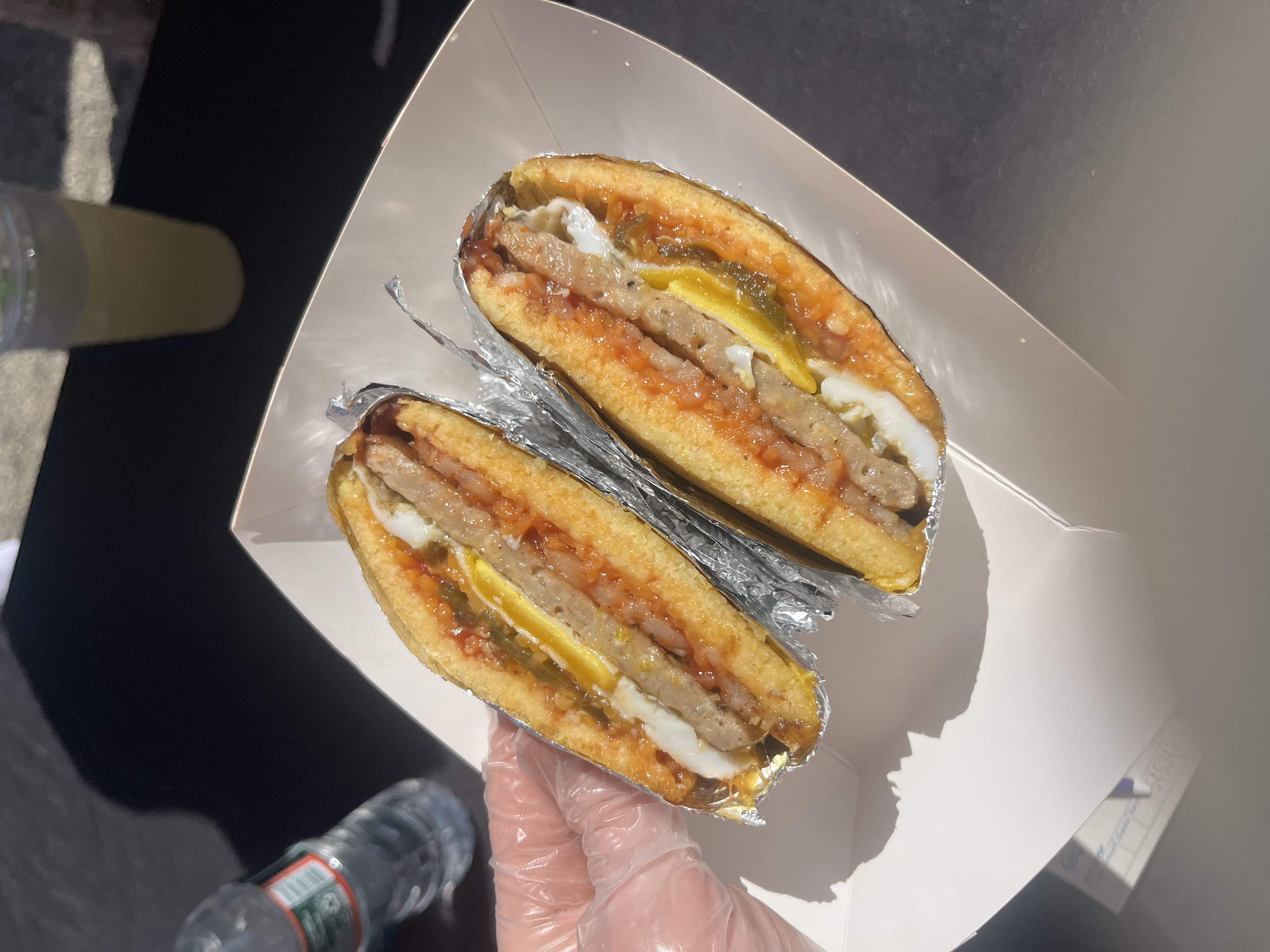 A gloved hand holding a sausage, egg and cheese arepa cut in half, shot live during service